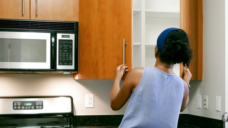 Woman opening brown wood kitchen cabinets.