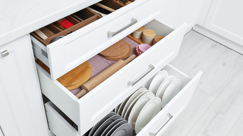 Three partially open, organized ktichen drawers holding cutlery, plates, and baking tools