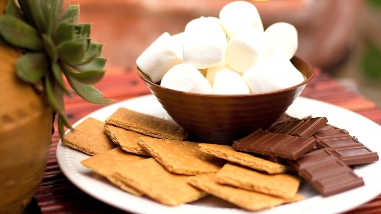 Small bowl of large marshmallows on a plate filled with graham crackers and chocolate bar pieces