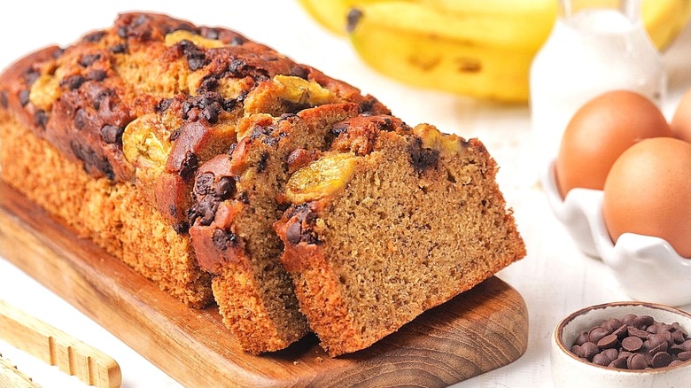 Loaf of pre-sliced banana bread with a chocolate and banana topping on a wooden serving board