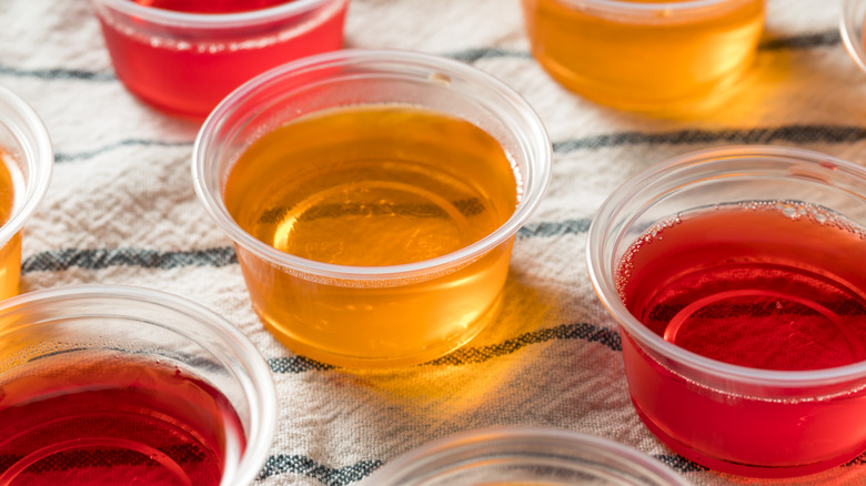 orange and red Jell-O shots in clear plastic containers on white striped cloth