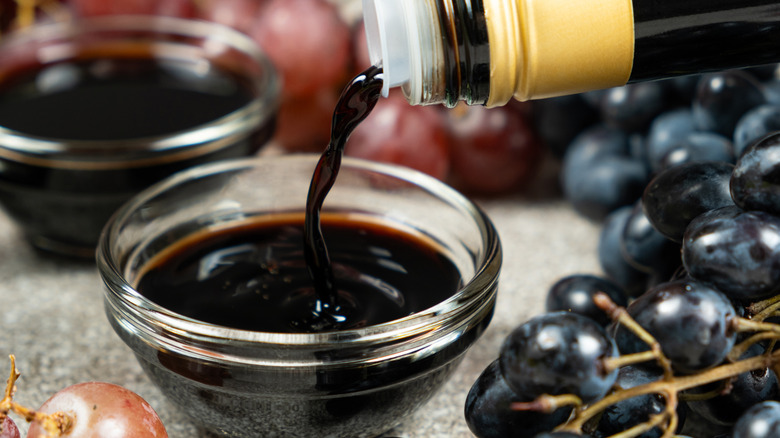 Balsamic vinegar is poured from a bottle into a small bowl.