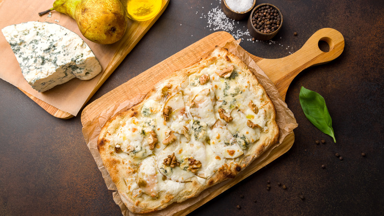 A gorgonzola-pear pizza next to a piece of gorgonzola, seen from above.