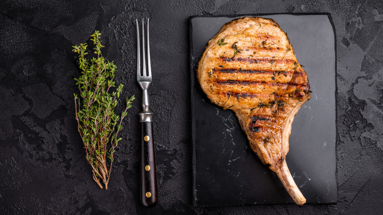 thyme, a fork, and a grilled pork chop on a black background