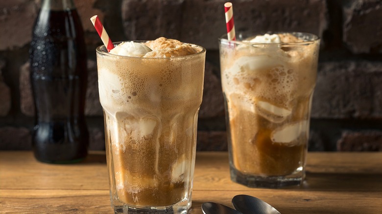 Two root beer floats in tall, clear glasses with red-and-white-striped straws