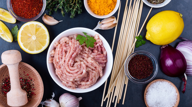 Ground poultry in a bowl surrounded by small pots of of vibrant spices and alliums.