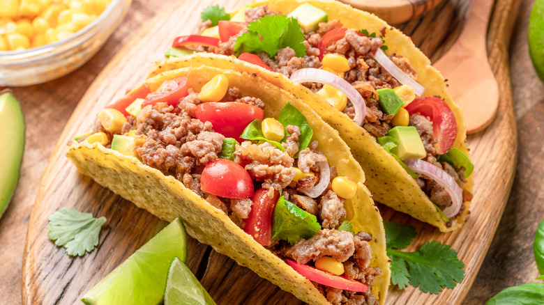tacos filled with meat and vegetables served on a wooden board