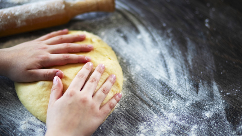 Hands working pasta dough on a floured surface