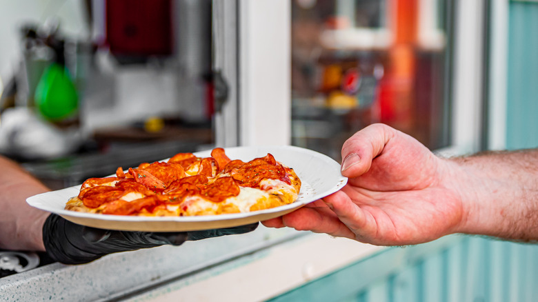 A person receiving their order of pepperoni pizza through a window