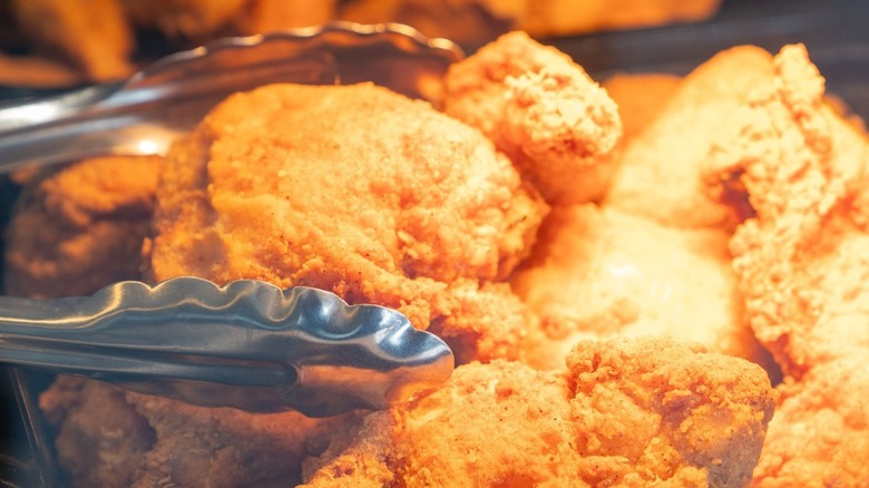 Tongs grabbing Golden Corral fried chicken off the buffet line