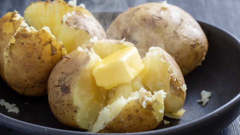 Baked potatoes topped with butter on a plate.