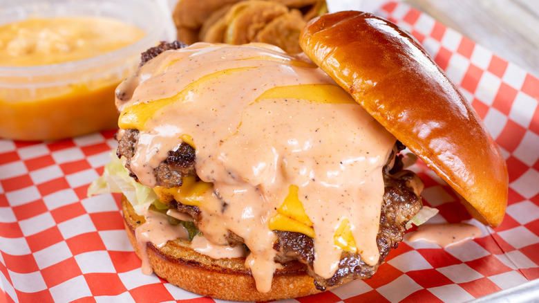 Double cheeseburger smothered in Thousand Island dressing, with the top bun removed but leaning against the burger stack