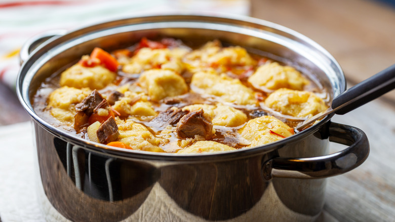 Beef, vegetables, and dumplings in metal pot with spoon.