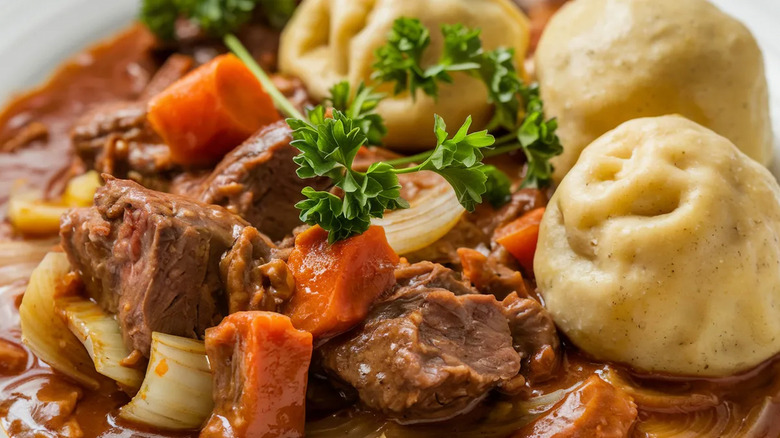 Beef, vegetables, and dumplings plated with fresh parsley.