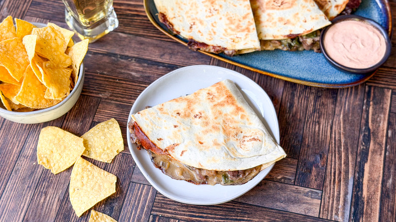 Gooey cheesesteak quesadillas on serving platter and plate with tortilla chips and dipping sauce