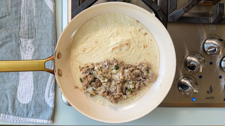 Large tortilla with gooey cheesesteak filling in skillet on stovetop