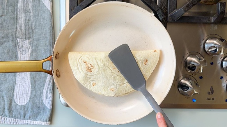 Using spatula to press down on gooey cheesesteak quesadilla in skillet on stovetop