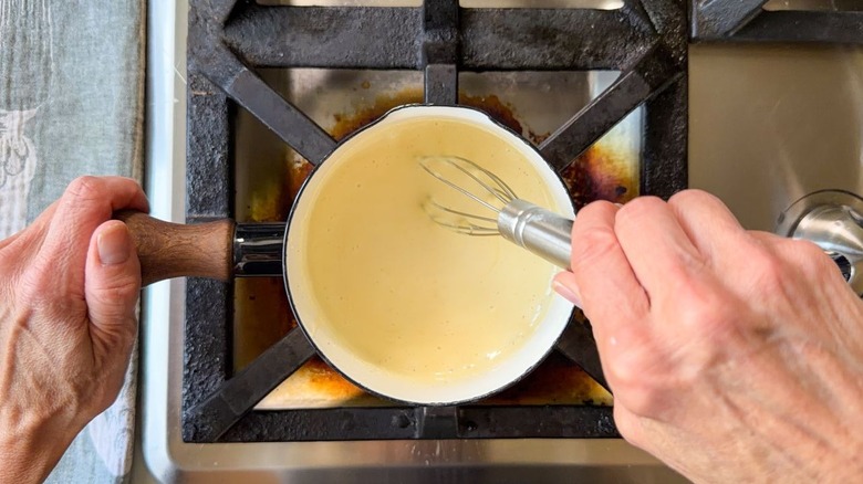 Whisking cheese sauce in small saucepan on stovetop