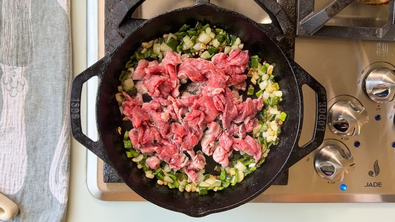 Raw shaved beef with peppers and onions in cast iron skillet on stovetop