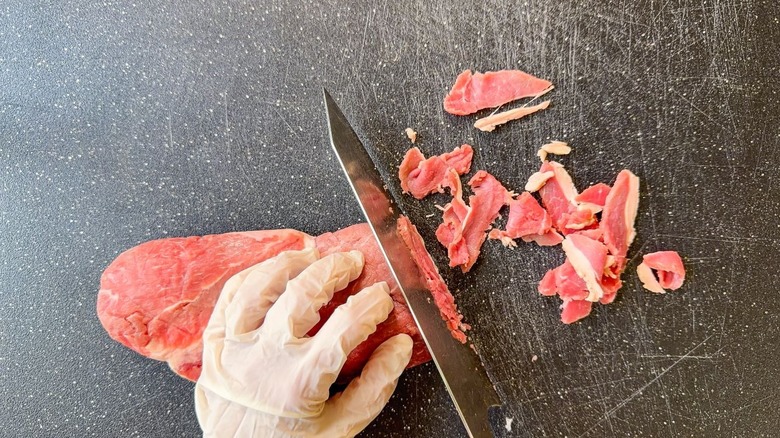Shaving beef slices from beef sirloin on cutting board