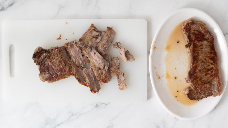 sliced cooked steak on a white board next to cooked steaks on a white plate
