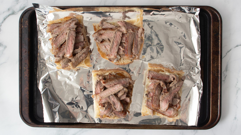 bread rolls with sliced steak on a foil-covered pan