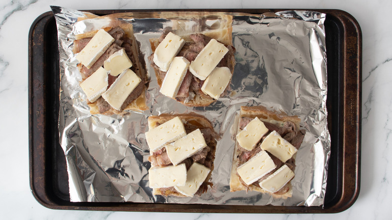 bread rolls with sliced steak and cheese on a foil-covered pan