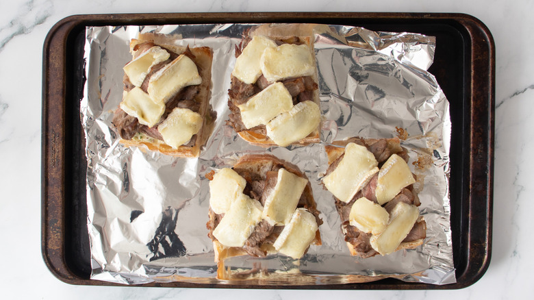 bread rolls with sliced steak and melted cheese on a foil-covered pan