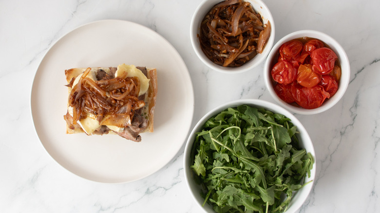 bread roll with steak, cheese, and fried shallots on a white plate