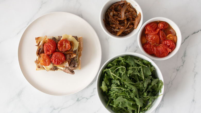 bread roll with steak, cheese, and tomatoes on a white plate