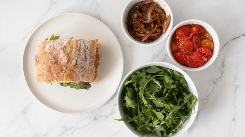 sandwich on a white plate next to vegetables in white bowls