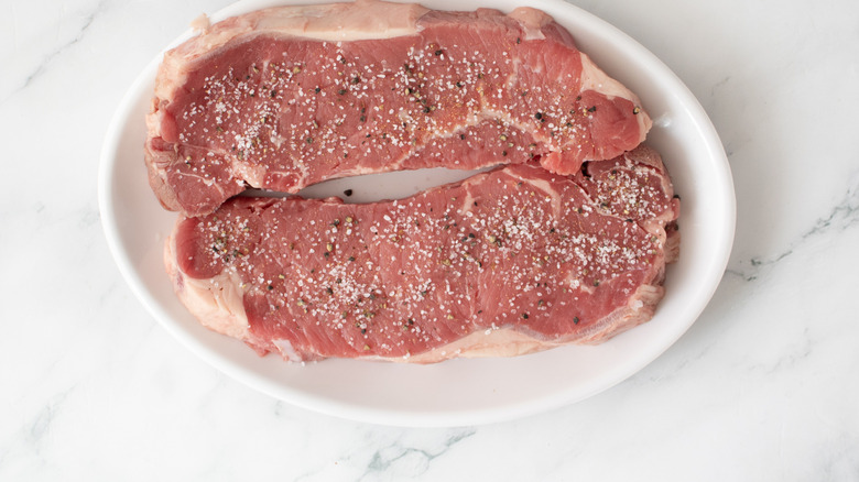 seasoned raw steaks on a white plate