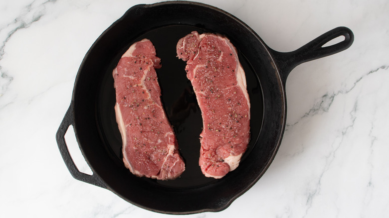 raw steaks in a black frying pan