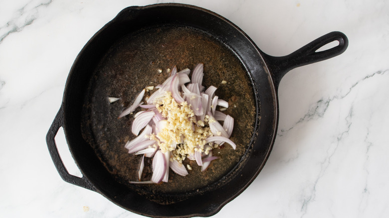raw garlic and shallots in a black frying pan