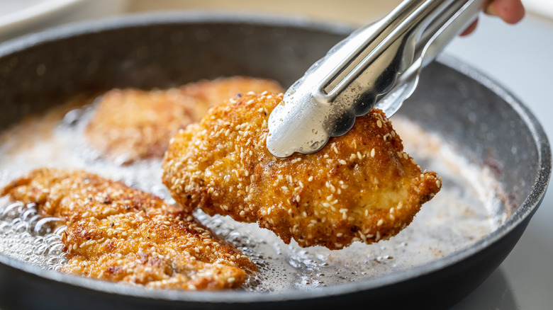 Three breaded chicken cutlets frying in a pan