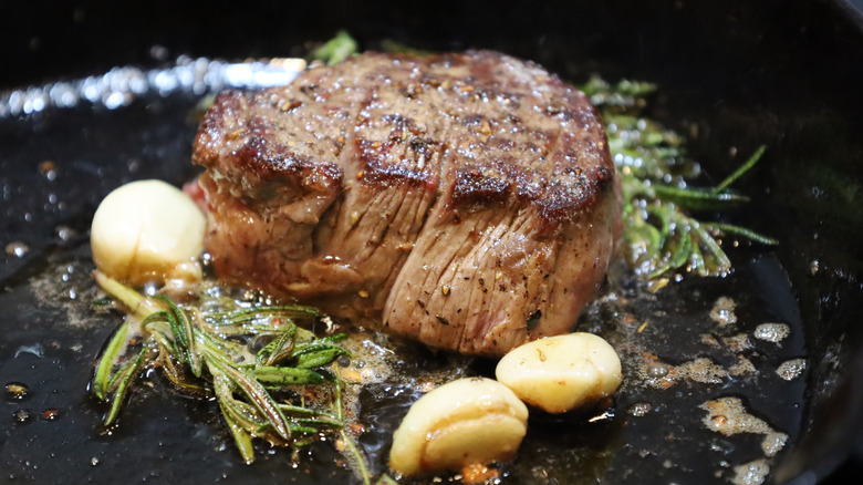 Lightly seared filet mignon in pan surrounded by rosemary and garlic
