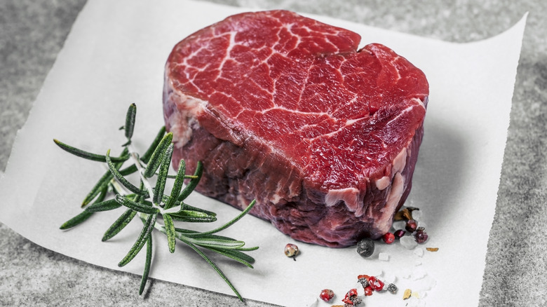 Raw filet mignon next to sprig of rosemary on parchment paper