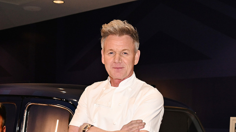 Gordon Ramsay smiling in a white chef jacket with his arms crossed