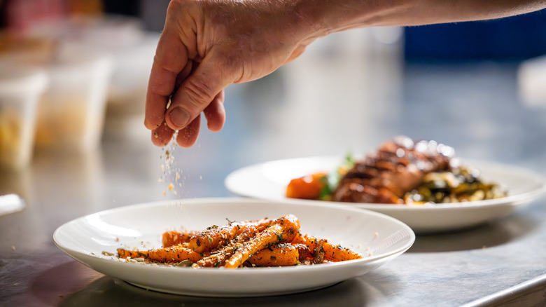 Hand sprinkling seasoning onto plate of carrots