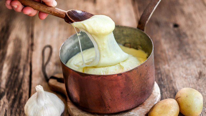 A person spooning out creamy pommes aligot out of a copper pot.