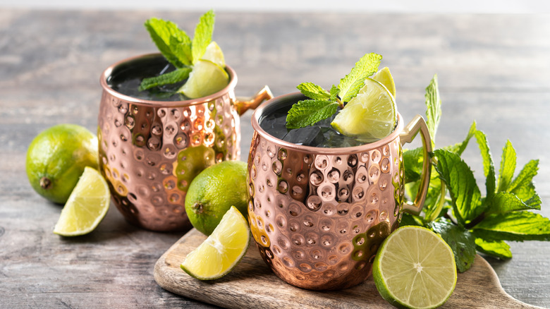 Two Moscow Mule cocktails in copper mugs garnished with lime and mint