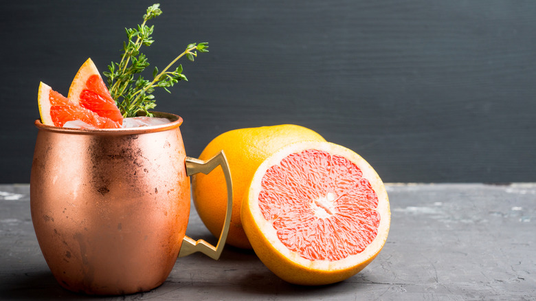 A grapefruit Moscow mule in a copper mug garnished with grapefruit wedges and herbs, next to a halved grapefruit