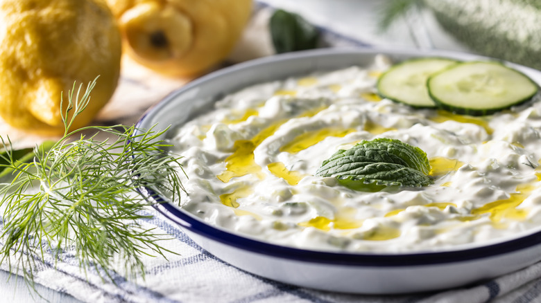 A bowl of tzatziki topped with cucumber slices and a mint leaf.