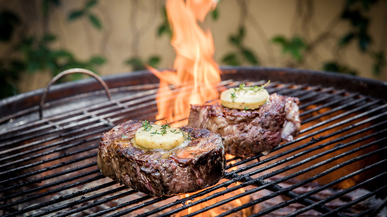Steaks topped with butter cooking on a charcoal grill