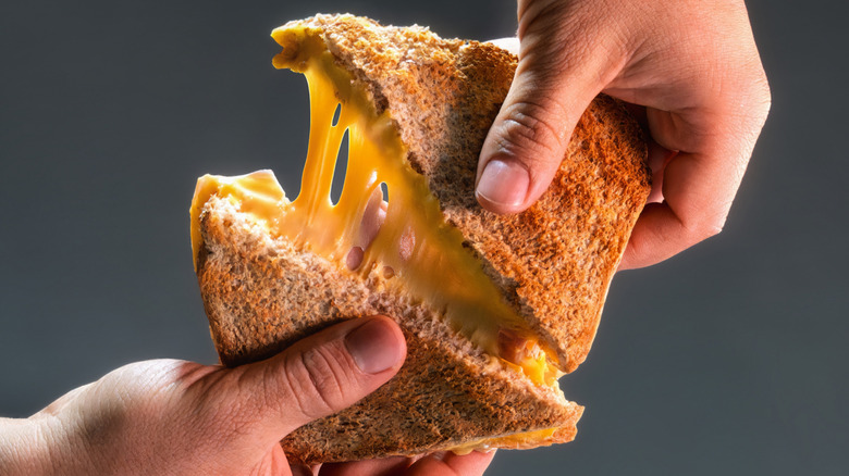 Delicious grilled cheese sandwich being pulled apart by hands.