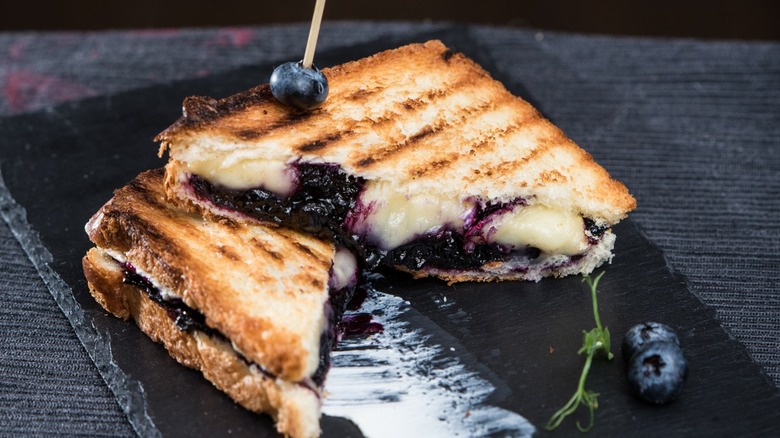 Grilled cheese sandwich filled with blueberry jam and brie cheese, cut in half on a gray slate plate
