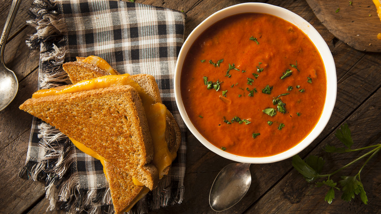 Grilled cheese sliced in half next to a bowl of tomato soup.