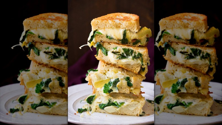 Spinach artichoke dip grilled cheese sandwiches sliced and stacked on a white plate