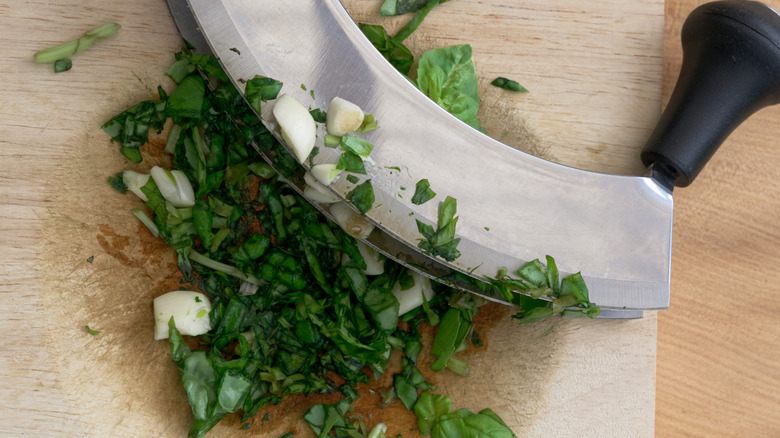 basil and garlic being chopped with mezzaluna