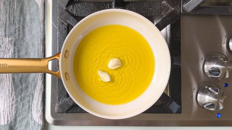 Garlic cloves cooking in olive oil in frying pan on stovetop